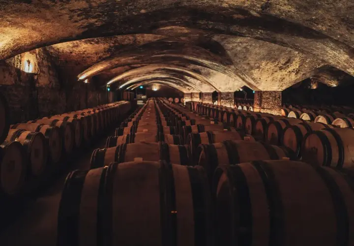 Cave voûtée remplie de rangées de fûts de chêne en bois.