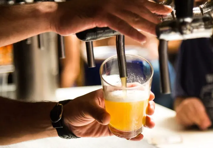 Main d'un homme servant une bière blonde dans un verre. Une question se pose : pourquoi la bière donne envie de faire pipi ?