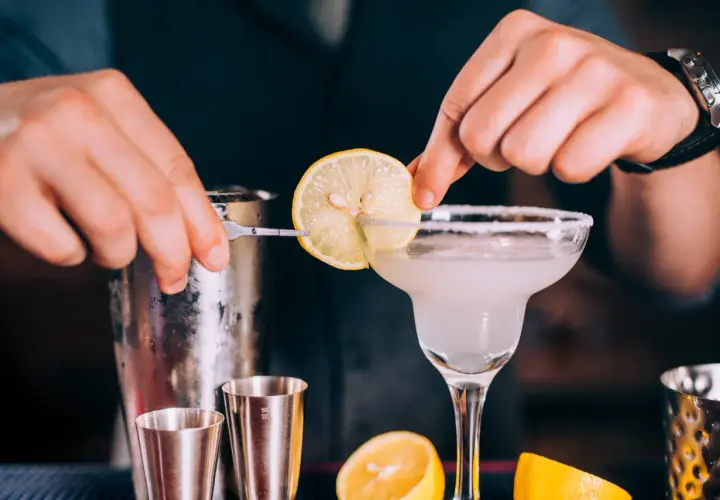 Un barman prépare un cocktail en p. avec une tranche de citron.