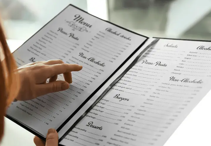 Une main parcourt le menu, cherchant le vin au verre parfait pour accompagner son repas.