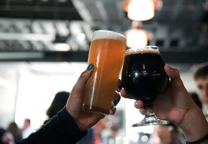 Deux mains lèvent des verres de bière, l'un blond et l'autre brun, pour un toast.