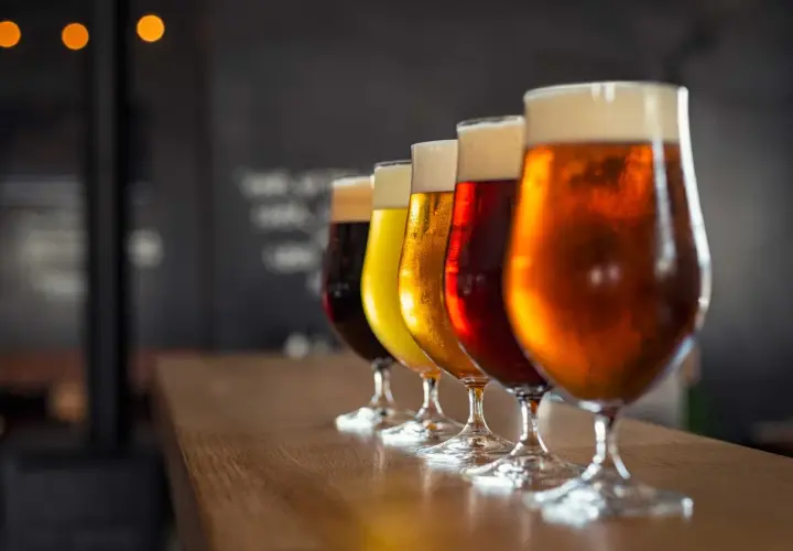 Une dégustation de différents types de bière, alignés sur un comptoir en bois. Les verres présentent des couleurs allant du blond doré au brun foncé, avec une mousse crémeuse.