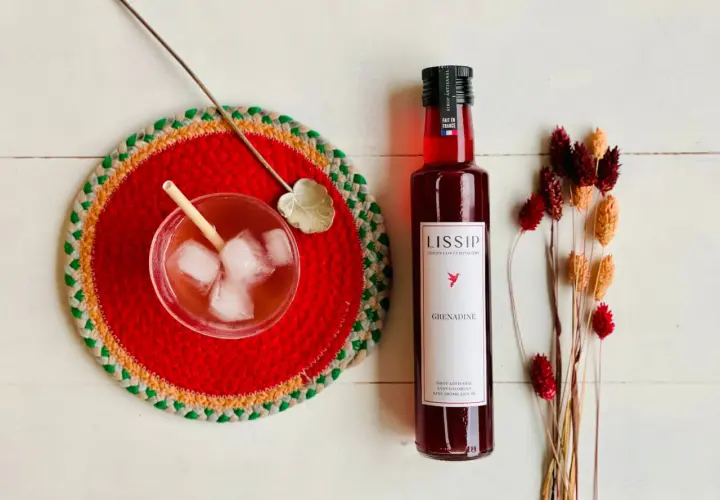 Un verre de boisson pétillante avec de la bière et de la grenadine, une bouteille de sirop de grenadine Lissip et des fleurs séchées.