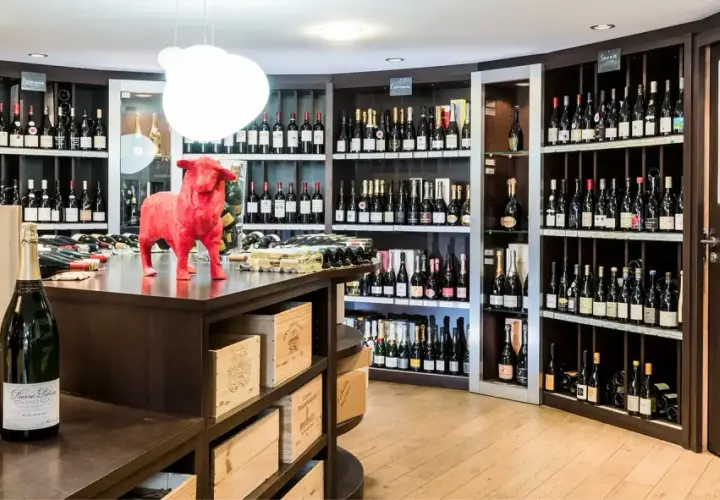 Cave à vin avec étagères remplies de bouteilles, une statue de taureau rouge et des bouteilles de champagne au premier plan.