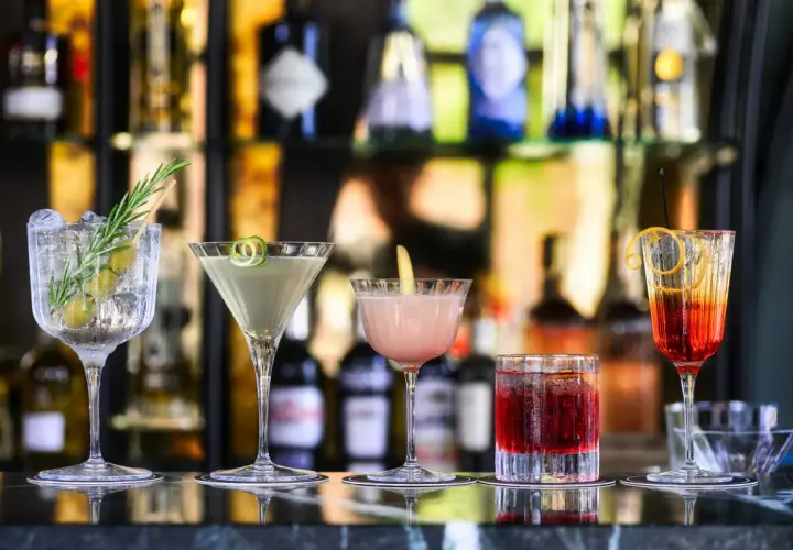 Cinq cocktails colorés, parfaits comme boisson pour ouvrir l'appétit, sont alignés sur un bar.