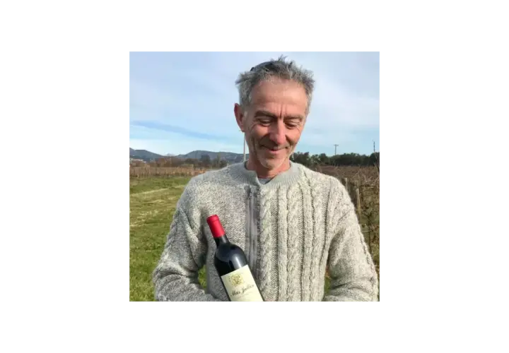 Un homme souriant tient une bouteille de vin Mas Jullien dans un vignoble.