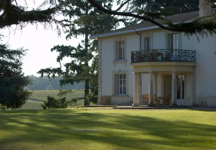 Le **château Pey la Tour** se dresse majestueusement, entouré de vignobles verdoyants sous un ciel clair. Une pelouse impeccable invite à la détente.
