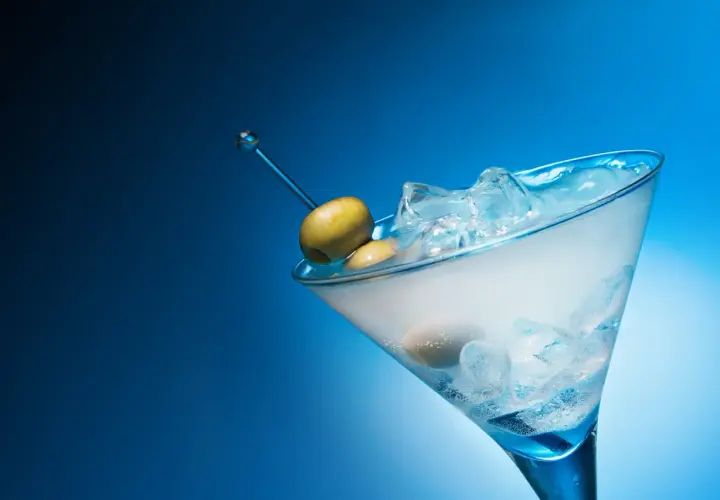 Un cocktail gin martini glacé, avec des olives sur un cure-dent bleu, sur fond bleu dégradé.