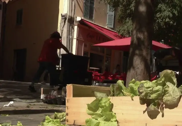 Des caisses de laitues fraîches attendent sur un trottoir, tandis que des personnes chargent des bacs. La duree fut de biere, mais le travail continue.
