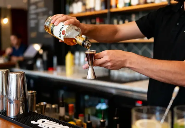 Un barman verse du whisky d'une bouteille dans un doseur. Il prépare un cocktail, prêt à boire à la bouteille ou au verre.