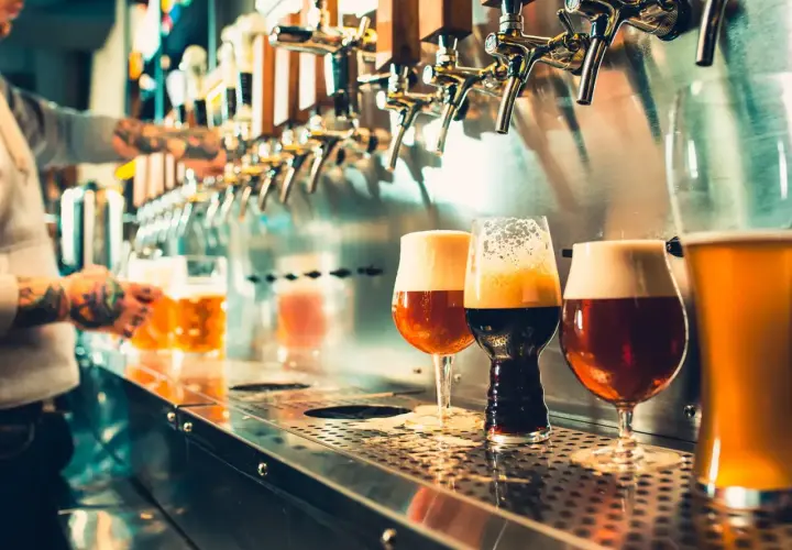 Verre de bière au bar, avec un barman en arrière-plan qui sert une chope.