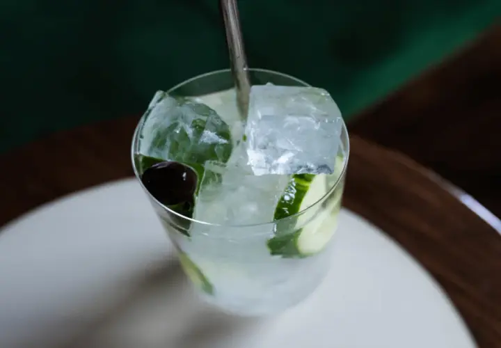 Un verre rempli de glaçons transparents, de rondelles de concombre et d'une cerise, prêt à être dégusté.