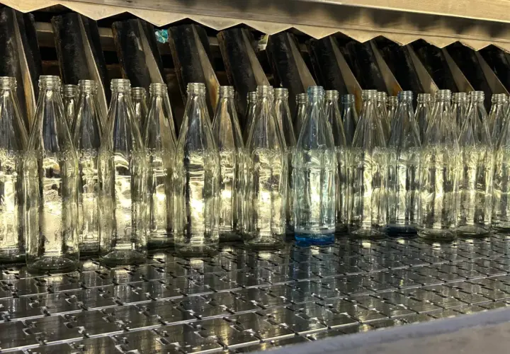 Une rangée de bouteilles en verre transparentes alignées sur une chaîne de production. On se demande combien de verre dans une bouteille d'eau.