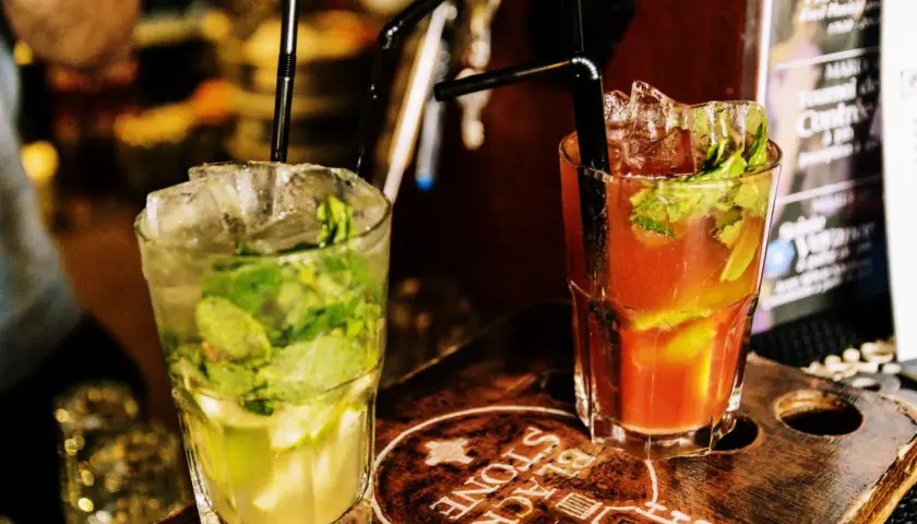 Deux cocktails rafraîchissants, un mojito vert et un autre rouge, sur un plateau en bois gravé.