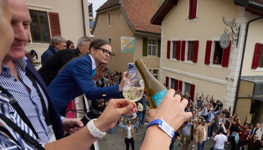 Une femme filme la plus grande bouteille du monde, d'où l'on verse du champagne dans un verre, devant une foule en liesse.