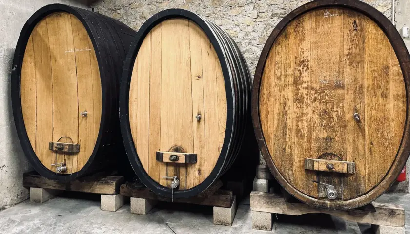 Trois fûts en bois de chêne, certains foncés, d'autres clairs, alignés dans une cave à vin.