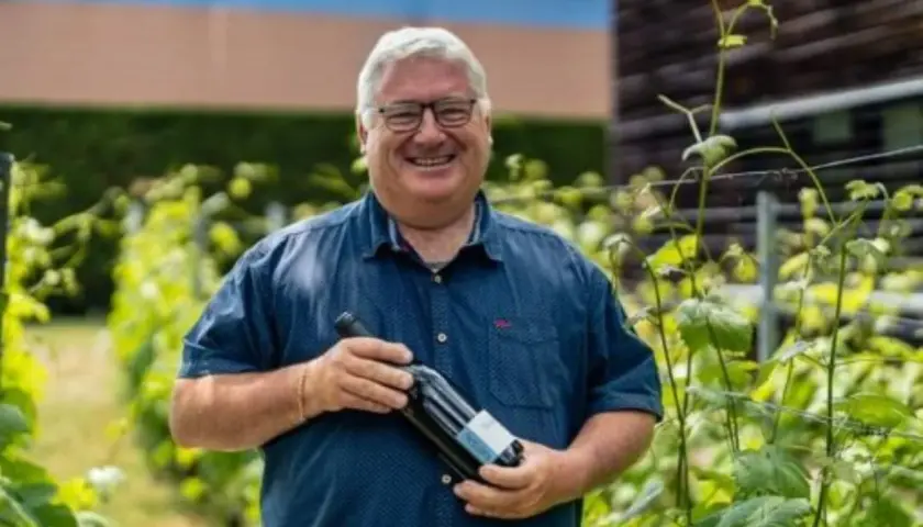 Un vigneron souriant tient une bouteille de vin dans les vignes du domaine du Trapadis.