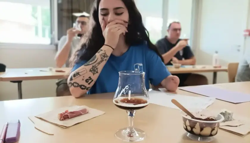 Jeune femme aux tatouages participe à une formation vin, dégustant une bière artisanale avec des accompagnements.