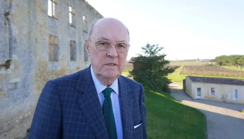 Alexandre de Lur Saluces, un homme d'affaires distingué, pose devant un château historique, les vignobles s'étendant à l'horizon.