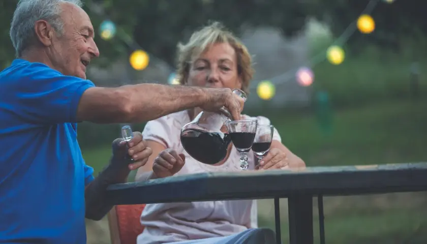 Un couple âgé profite d'un verre de vin par jour dans le jardin, sous des guirlandes lumineuses.