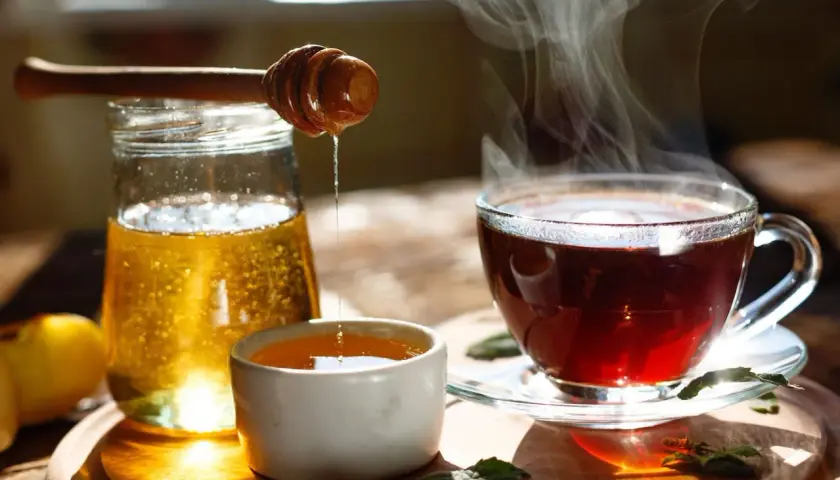 Une boisson eau et miel fumante, avec un pot de miel et une cuillère en bois dégoulinant.