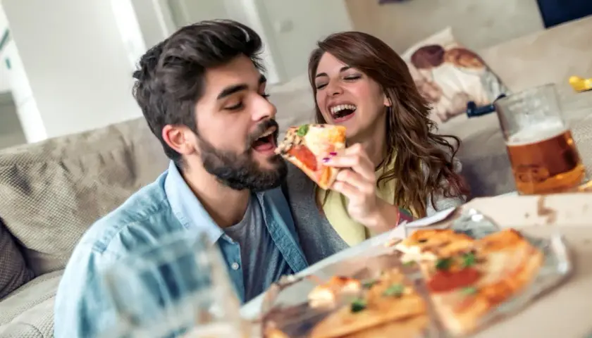 Un couple partage une pizza et de la bière, oubliant le régime pour un moment de plaisir gourmand.