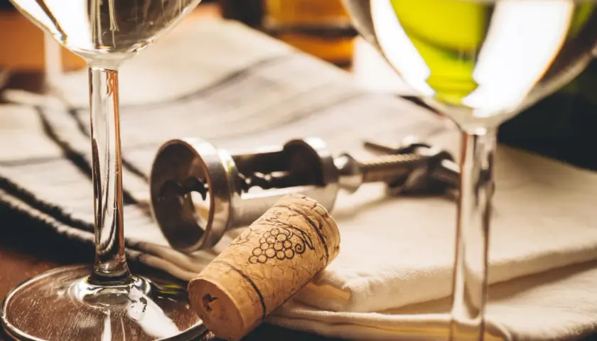 Deux verres de vin blanc, un tire-bouchon et un bouchon orné de grappes de raisin. Le droit de bouchon prix est souvent discuté lors de dégustations.