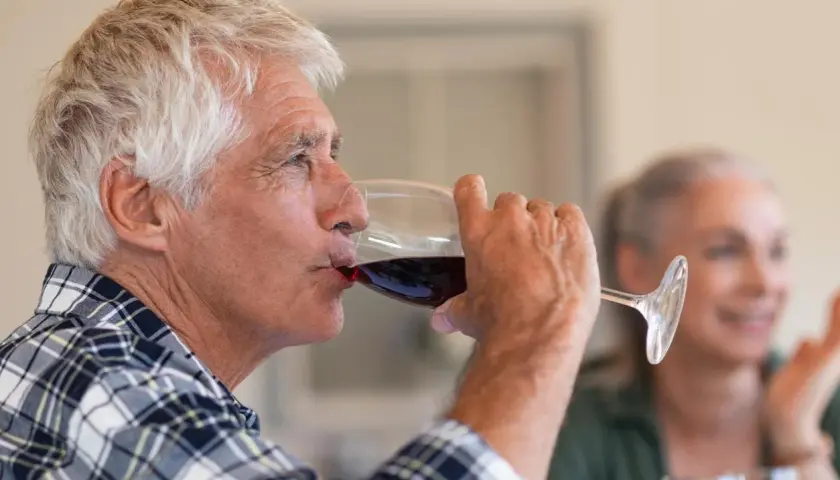 Un homme âgé boit du vin rouge. Attention, le vin périmé présente un danger.