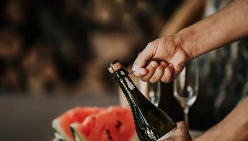 Main tenant du goulot, une main dépose délicatement le muselet. La clé pour savoir comment ouvrir une bouteille de champagne est dans ce geste précis.