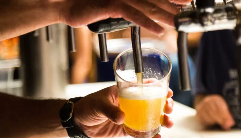 Main d'un homme servant une bière blonde dans un verre. Une question se pose : pourquoi la bière donne envie de faire pipi ?