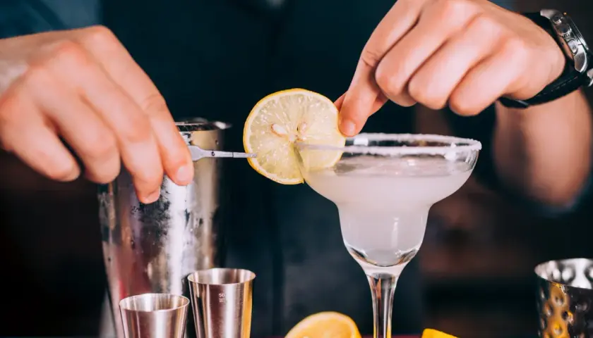 Un barman prépare un cocktail en p. avec une tranche de citron.