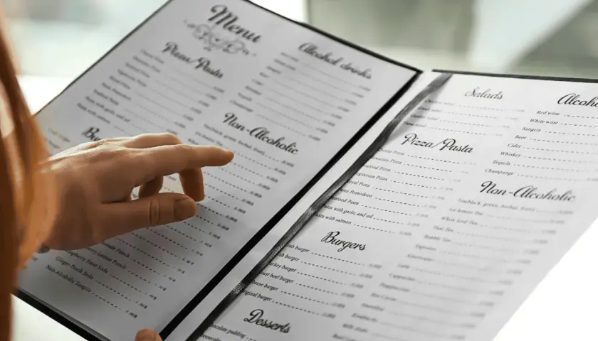 Une main parcourt le menu, cherchant le vin au verre parfait pour accompagner son repas.