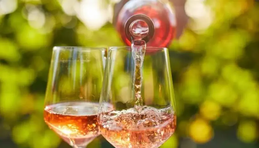 Un verre de rosé est servi dans un autre verre, sous un soleil radieux. Un moment parfait pour boire du rosé tous les jours.