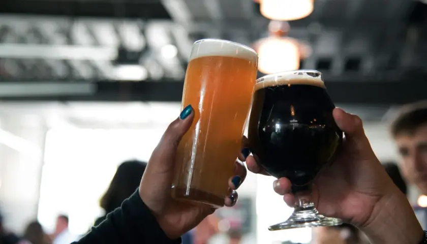 Deux mains lèvent des verres de bière, l'un blond et l'autre brun, pour un toast.