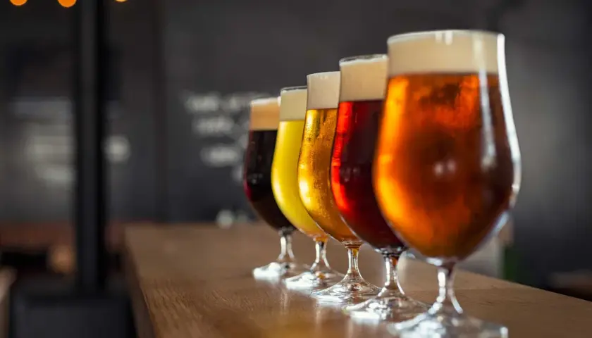 Une dégustation de différents types de bière, alignés sur un comptoir en bois. Les verres présentent des couleurs allant du blond doré au brun foncé, avec une mousse crémeuse.