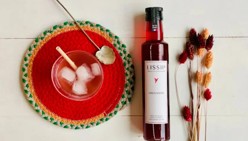 Un verre de boisson pétillante avec de la bière et de la grenadine, une bouteille de sirop de grenadine Lissip et des fleurs séchées.