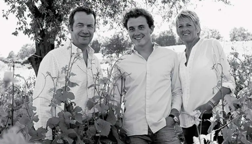 Trois générations de la famille Arnoux Lachaux sourient dans un vignoble, entourés de vignes.