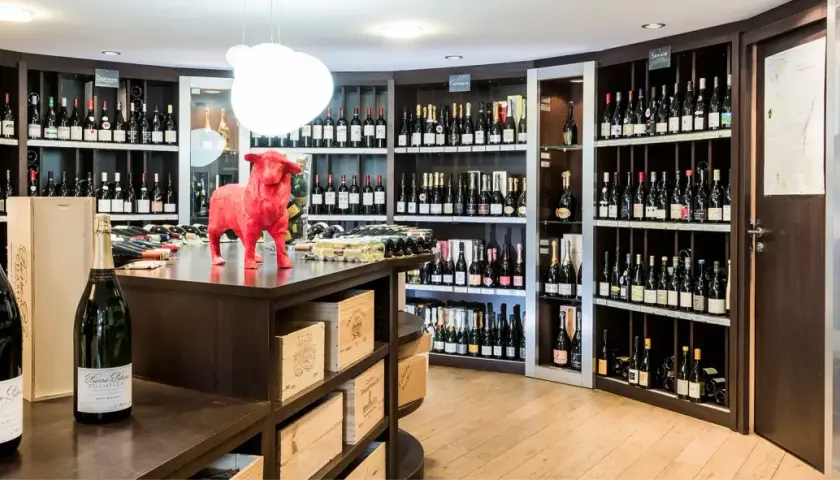 Cave à vin avec étagères remplies de bouteilles, une statue de taureau rouge et des bouteilles de champagne au premier plan.