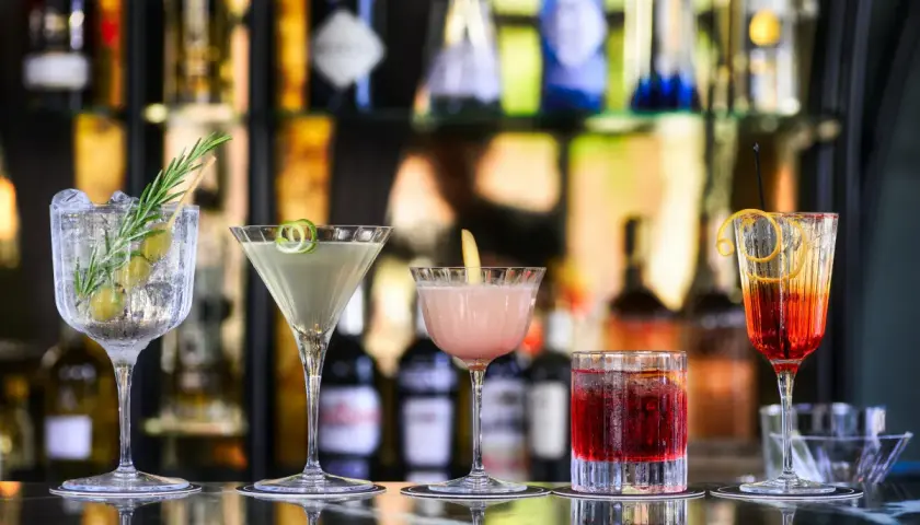 Cinq cocktails colorés, parfaits comme boisson pour ouvrir l'appétit, sont alignés sur un bar.