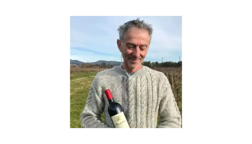 Un homme souriant tient une bouteille de vin Mas Jullien dans un vignoble.