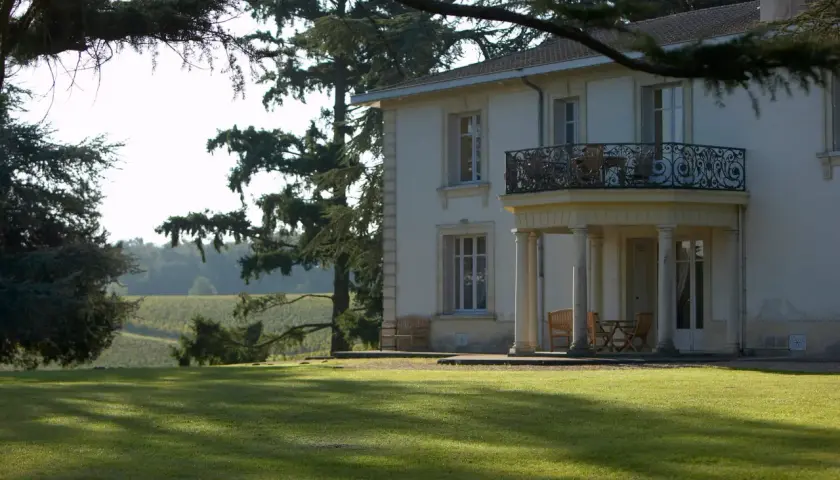 Le **château Pey la Tour** se dresse majestueusement, entouré de vignobles verdoyants sous un ciel clair. Une pelouse impeccable invite à la détente.