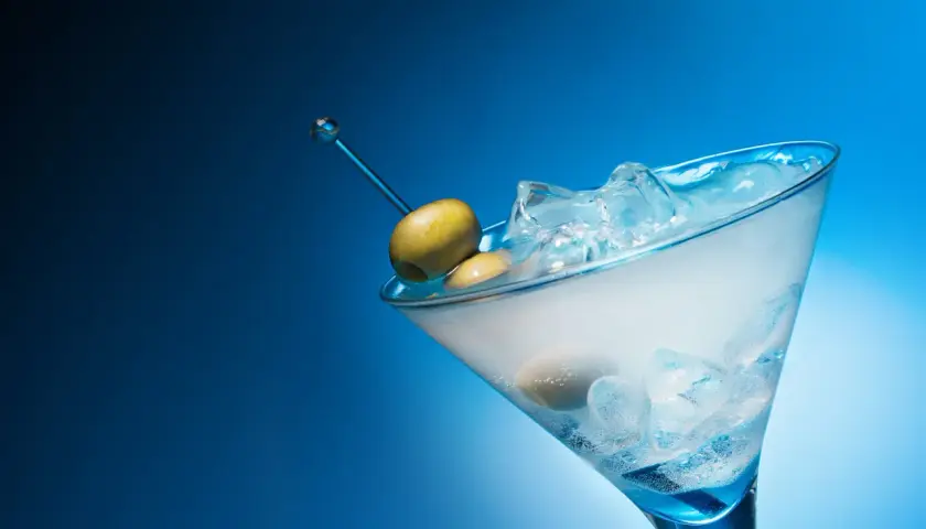 Un cocktail gin martini glacé, avec des olives sur un cure-dent bleu, sur fond bleu dégradé.