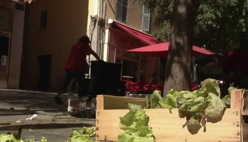 Des caisses de laitues fraîches attendent sur un trottoir, tandis que des personnes chargent des bacs. La duree fut de biere, mais le travail continue.