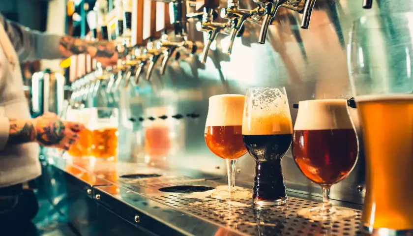 Verre de bière au bar, avec un barman en arrière-plan qui sert une chope.