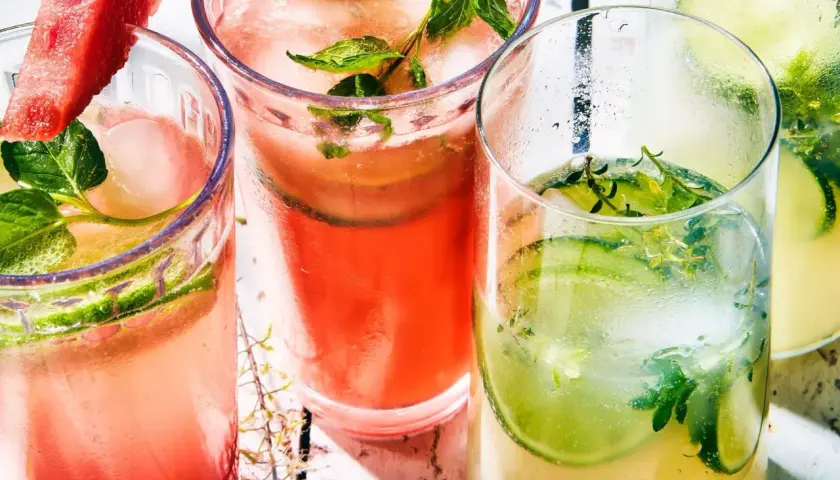 Trois verres de cocktail classique, garni de concombre, menthe et pastèque, sur un fond clair.