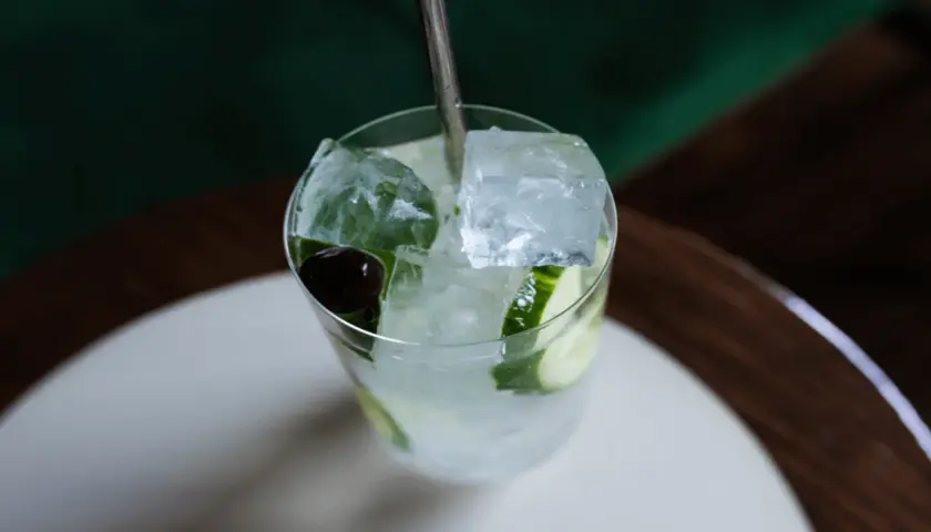 Un verre rempli de glaçons transparents, de rondelles de concombre et d'une cerise, prêt à être dégusté.