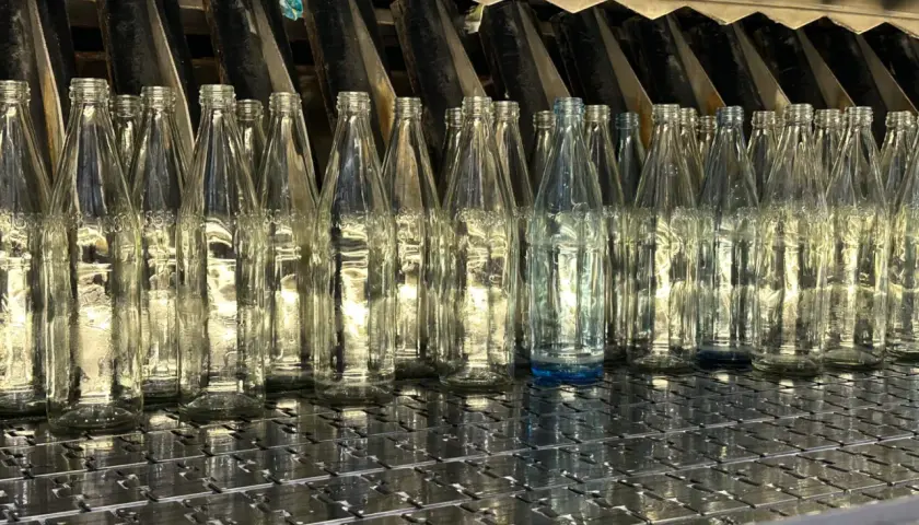 Une rangée de bouteilles en verre transparentes alignées sur une chaîne de production. On se demande combien de verre dans une bouteille d'eau.