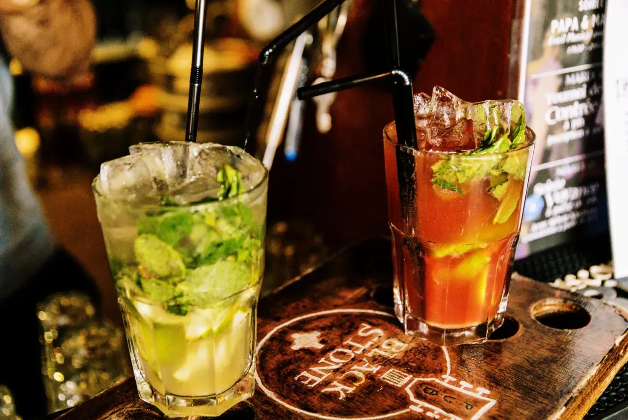 Deux cocktails rafraîchissants, un mojito vert et un autre rouge, sur un plateau en bois gravé.