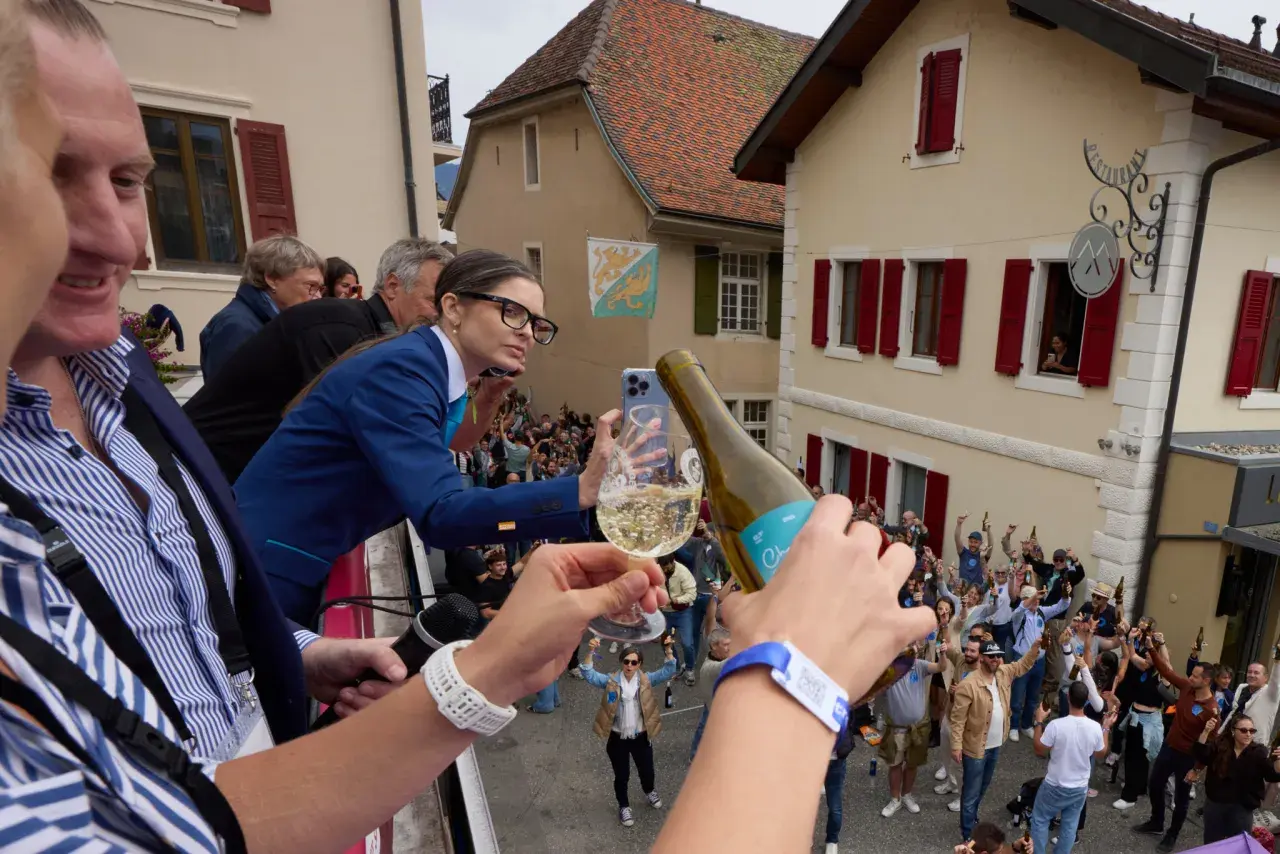 Une femme filme la plus grande bouteille du monde, d'où l'on verse du champagne dans un verre, devant une foule en liesse.