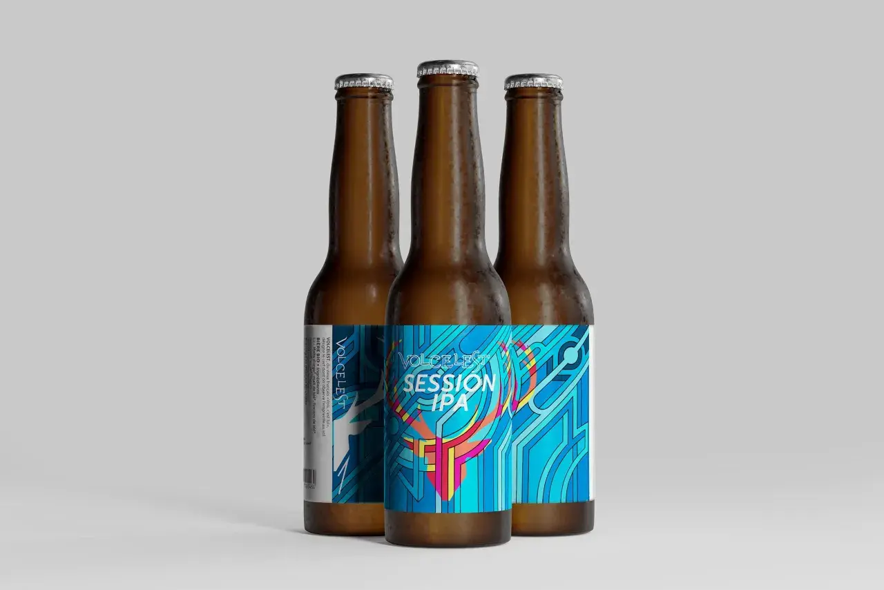Trois bouteilles de bière ambrée, dont une avec une étiquette colorée "VOLCELEST SESSION IPA" aux motifs géométriques bleus et roses.